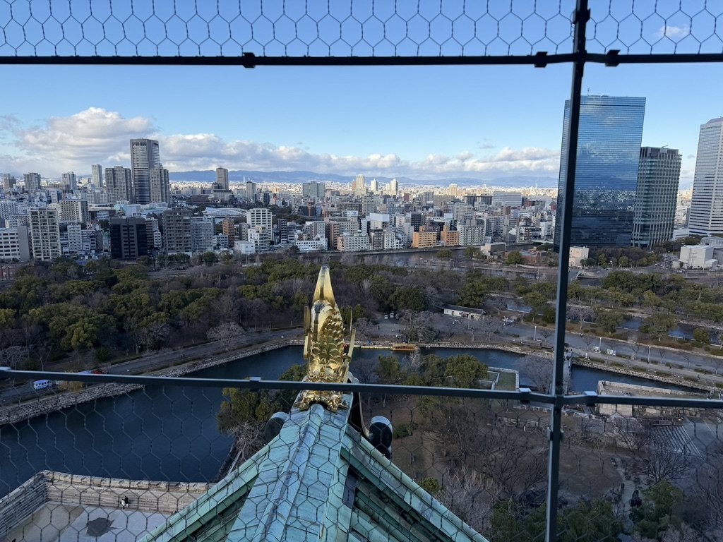 A gilded shachihoko on the castle roof, with the moat and city below