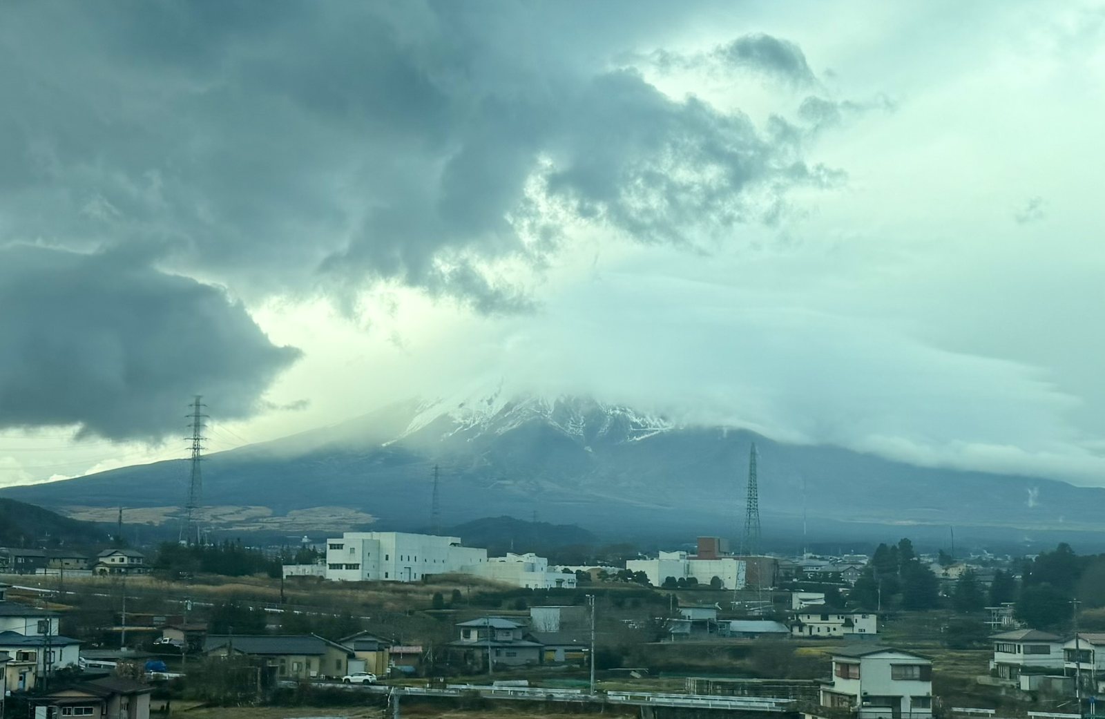 Mt Fuji wrapped in heavy cloud, with snow on its upper slopes and houses in the foreground