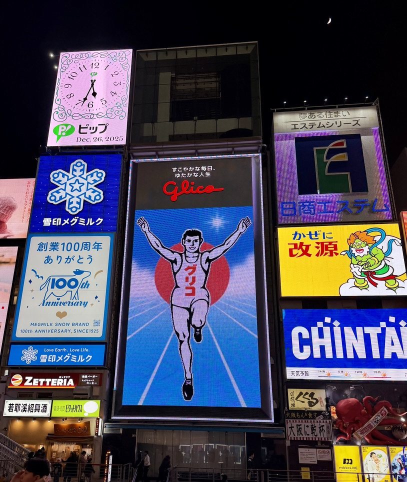 The Glico running-man billboard in Dōtonbori at night, with a clock reading Dec. 26, 2025