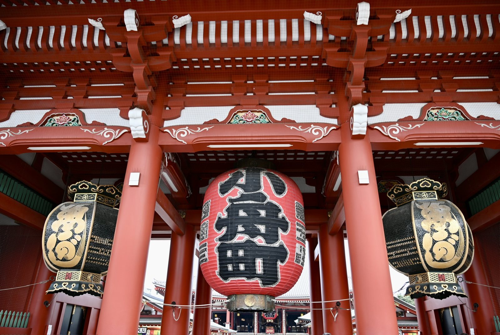 A huge red paper lantern hanging in the vermilion Hōzōmon gate of Sensō-ji, flanked by two black-and-gold lanterns