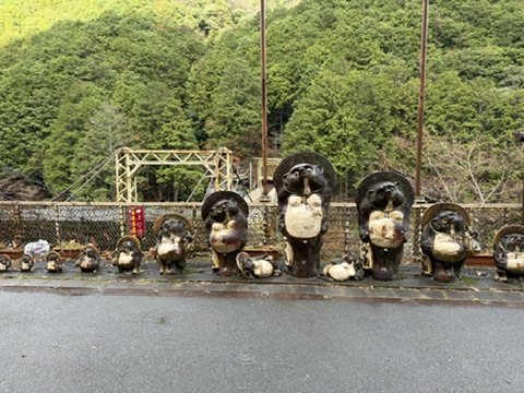 A row of ceramic tanuki statues on a station platform above a river gorge