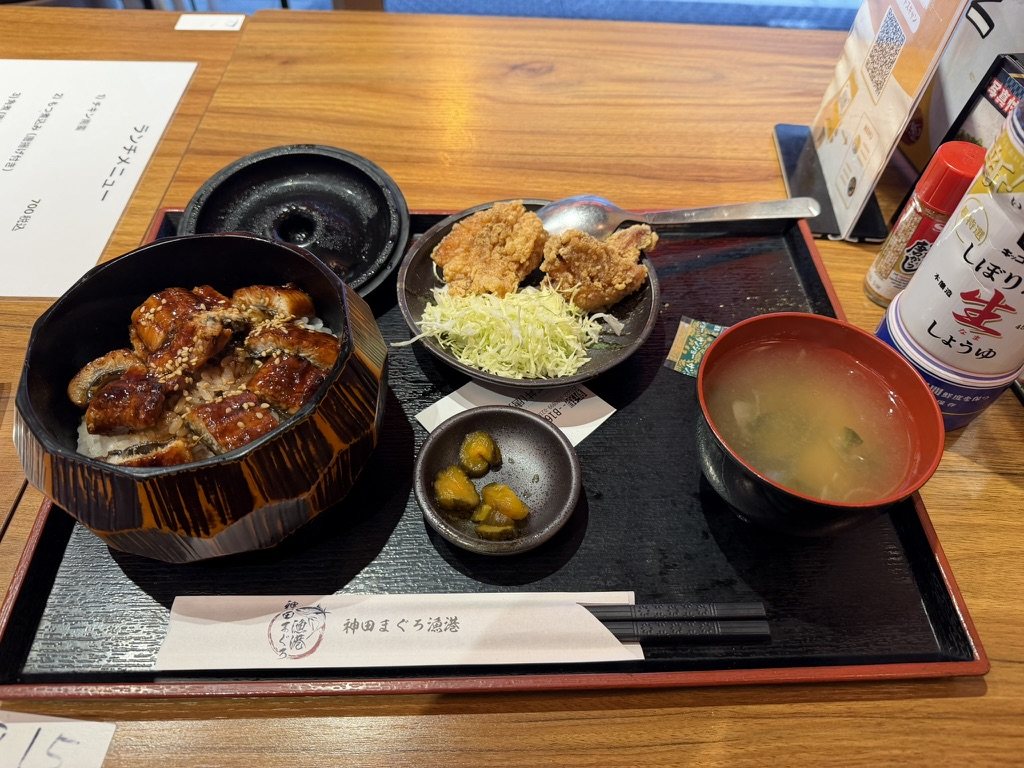 A lacquered bowl of grilled eel over rice, with fried chicken, miso soup, and pickles on a tray