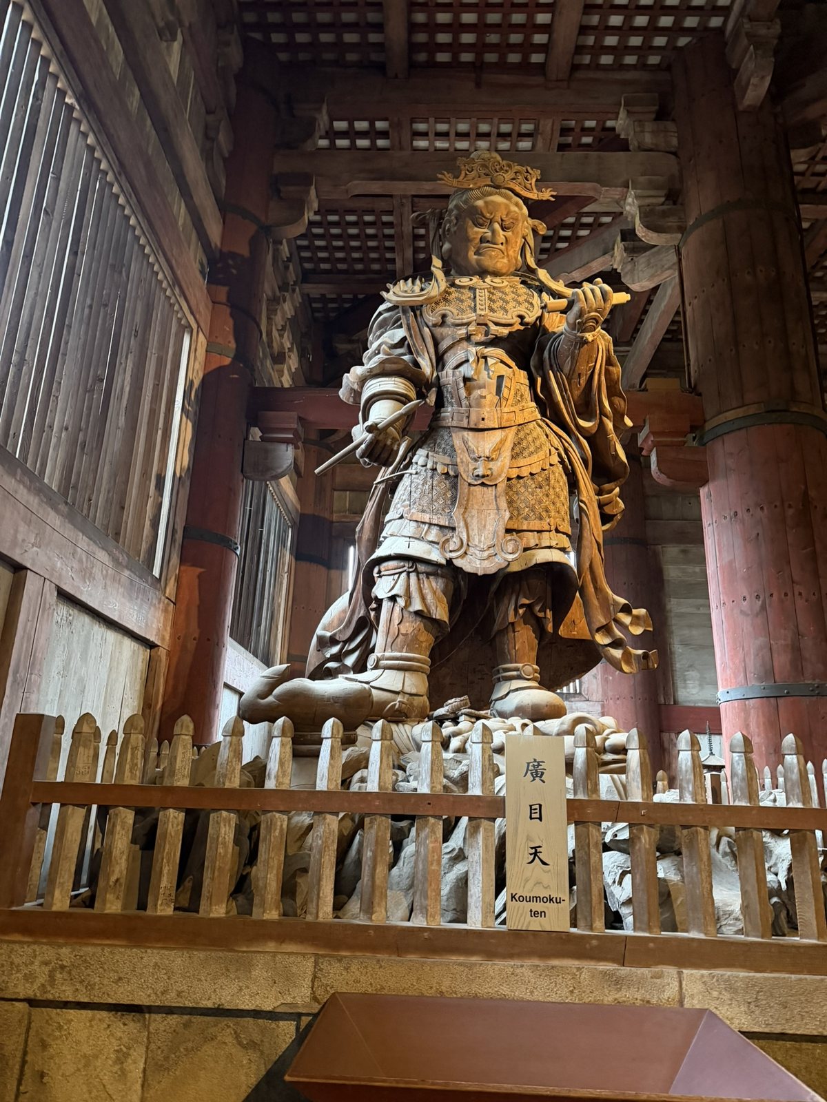 A large wooden statue of the guardian Kōmokuten in armor