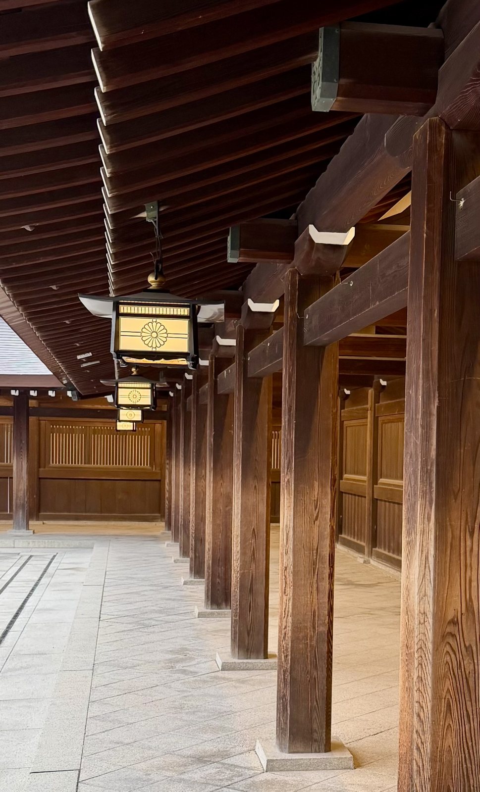 A wooden colonnade with hanging lanterns bearing the chrysanthemum crest