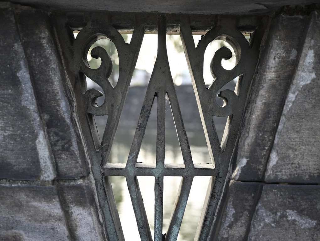 An old iron grille set in stone, with the palace moat blurred behind it
