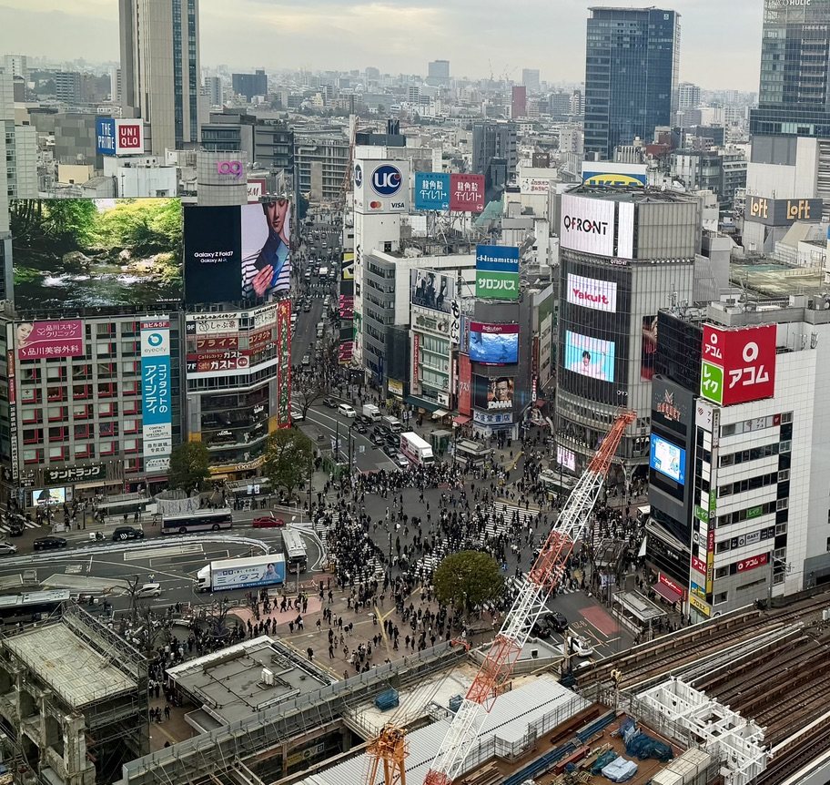 The Shibuya scramble crossing from above, full of people, surrounded by billboards