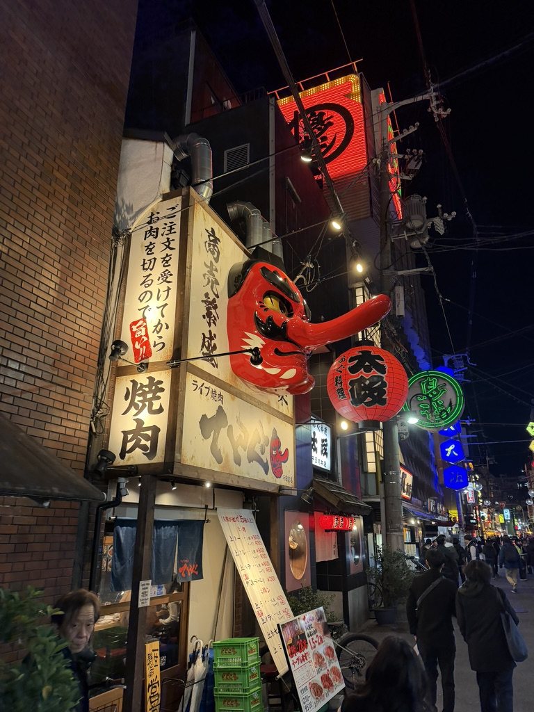 A large red tengu mask over a yakiniku restaurant in Shinsekai