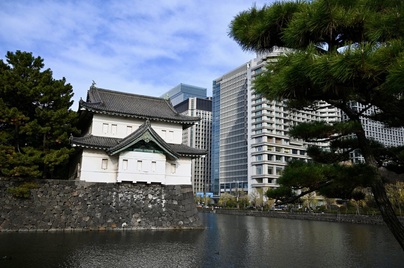 A white two-story Edo Castle corner turret on a stone wall above the moat, with office towers behind