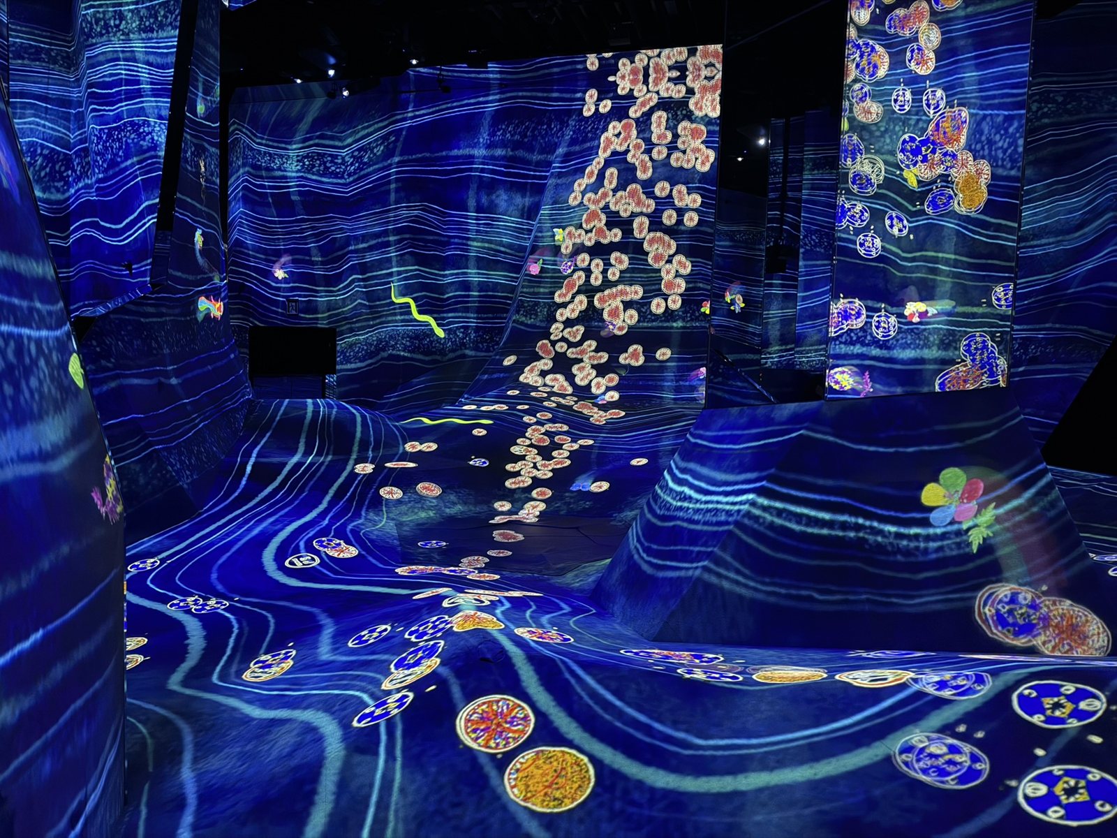 A room at teamLab Planets with blue projected light and drifting flower-like shapes across sloped walls and floor
