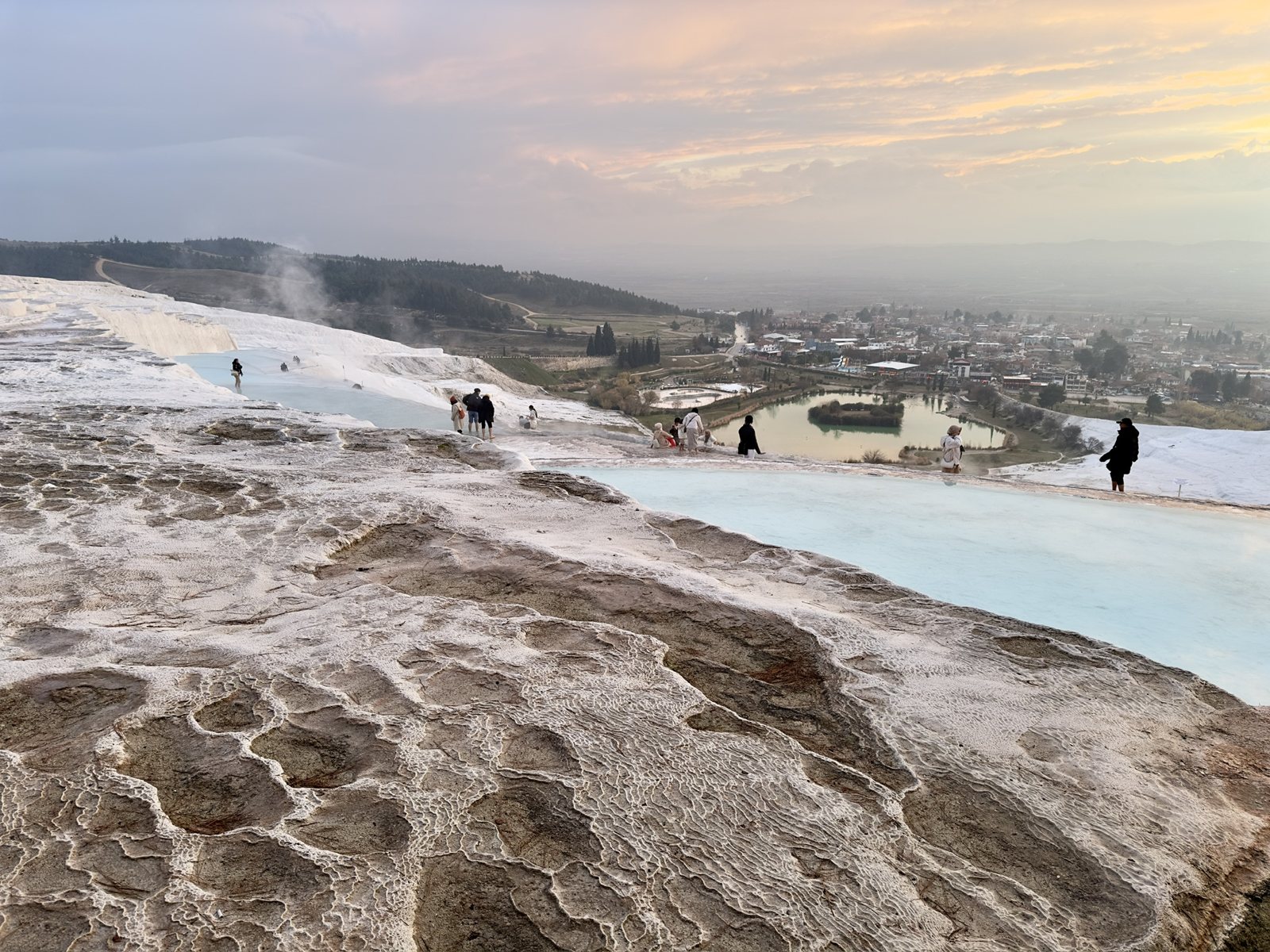 Turquoise pools on the white travertine terraces of Pamukkale, with the village and a lake below