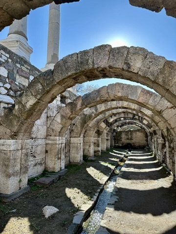 Stone arches receding in a row in the vaulted basement of the Agora of Smyrna, with a water channel along the floor