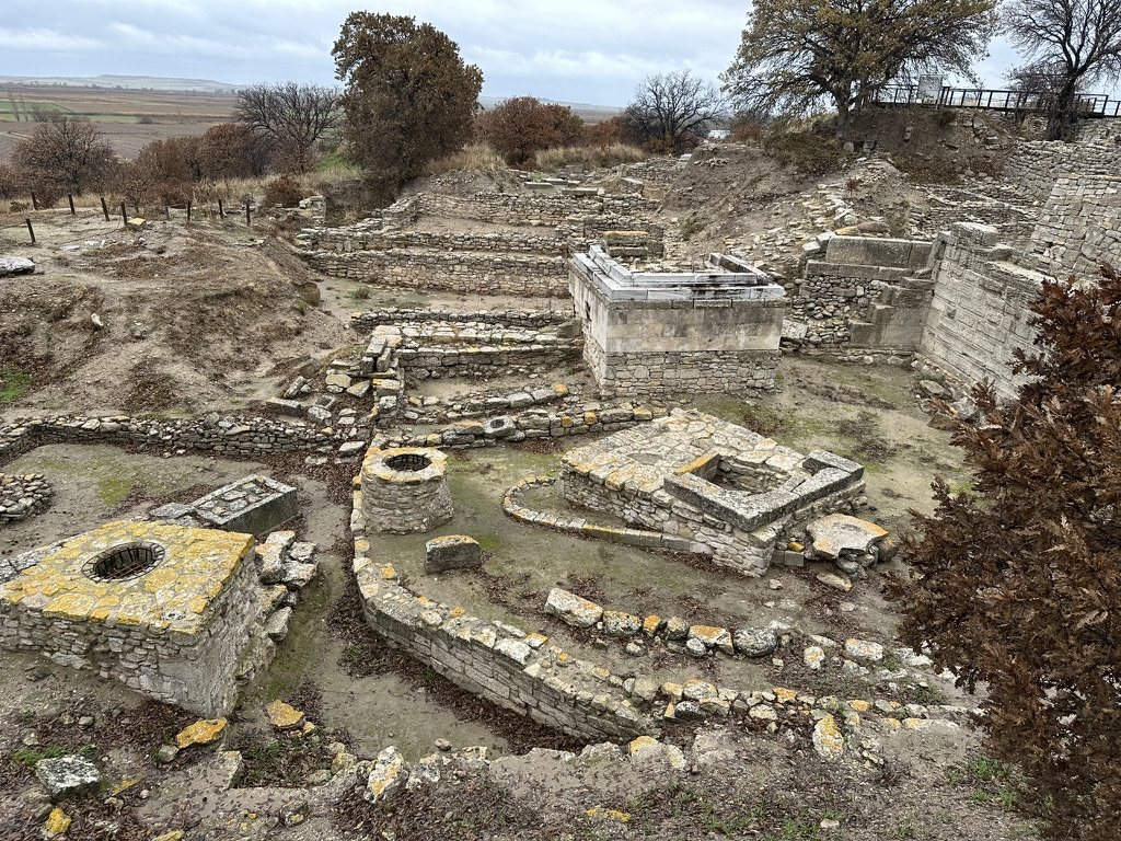Stone wells and altars among older walls at Troy